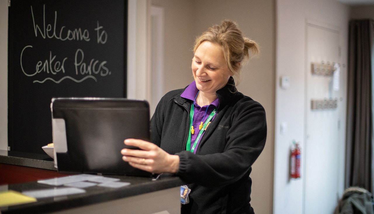 A woman in the purple Center Parcs uniform with a chalkboard saying 'Welcome to Center Parcs' in the background