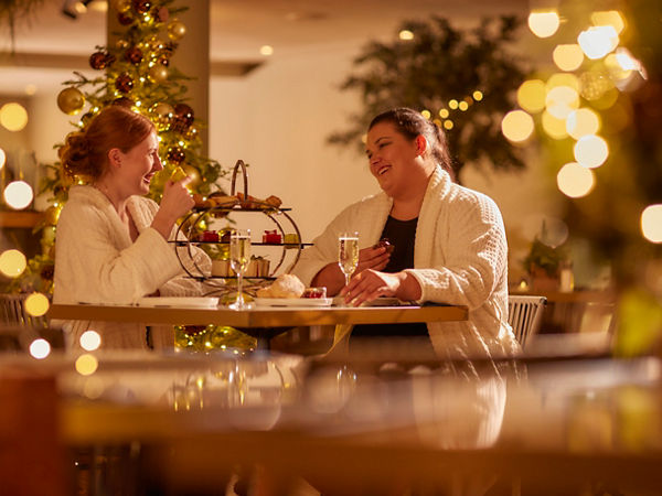 two women sat at a table in spa robes with christmas lights and decorations around the room