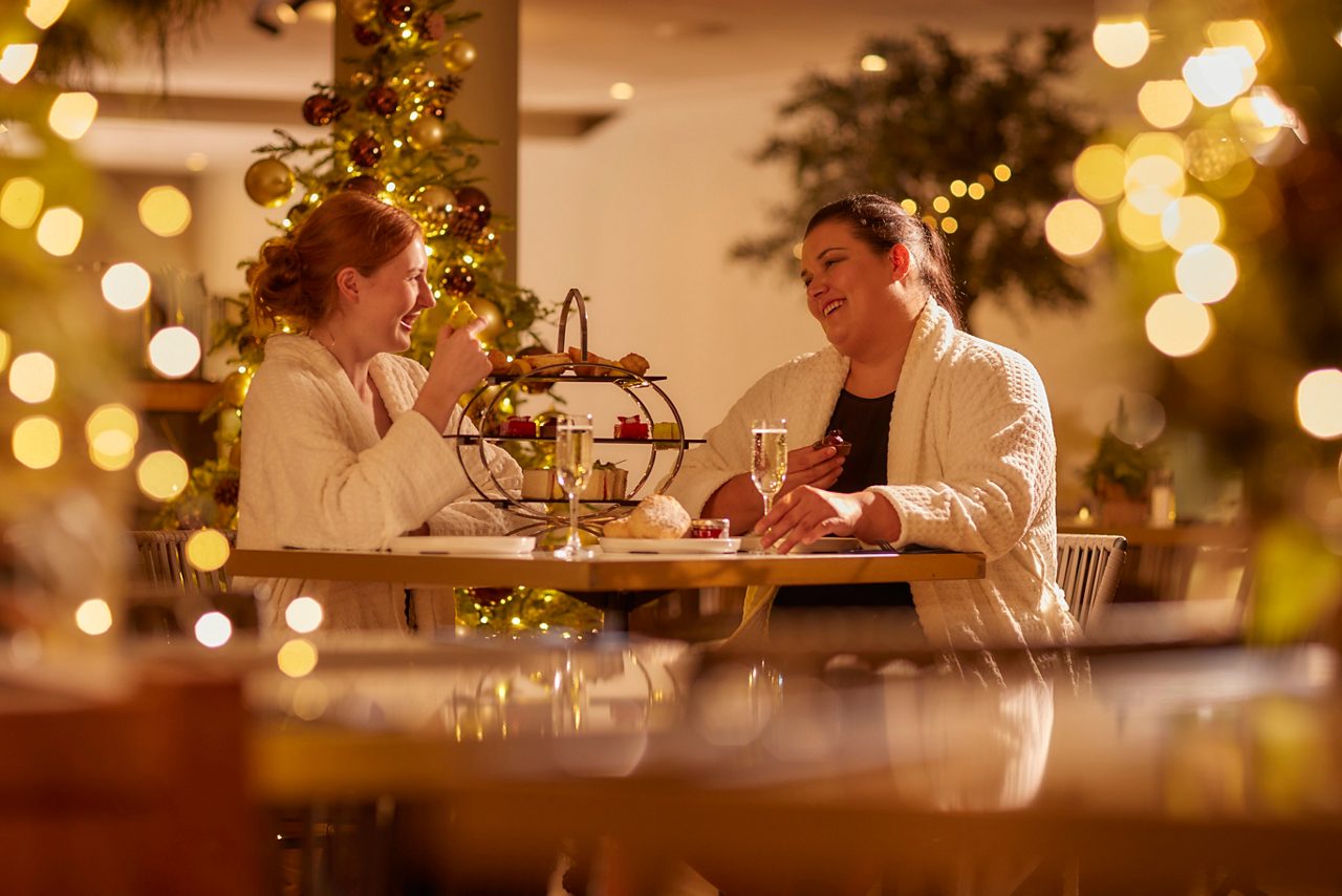two women sat at a table in spa robes with christmas lights and decorations around the room