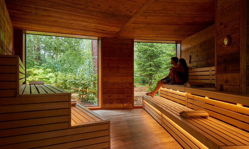 Couple sitting in the Nordic Sauna enjoying views of the forest.