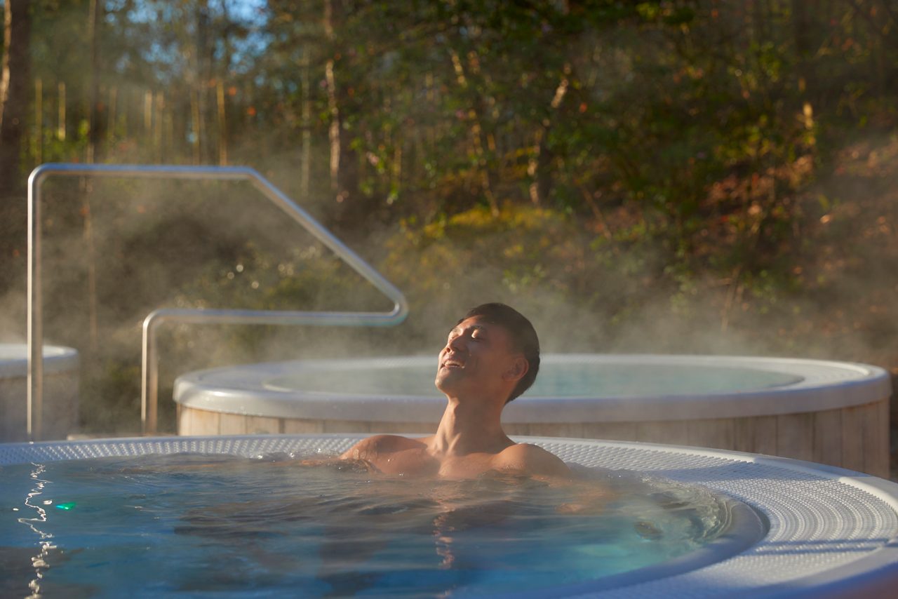 Man soaking in a steamy hot tub surrounded by the forest.