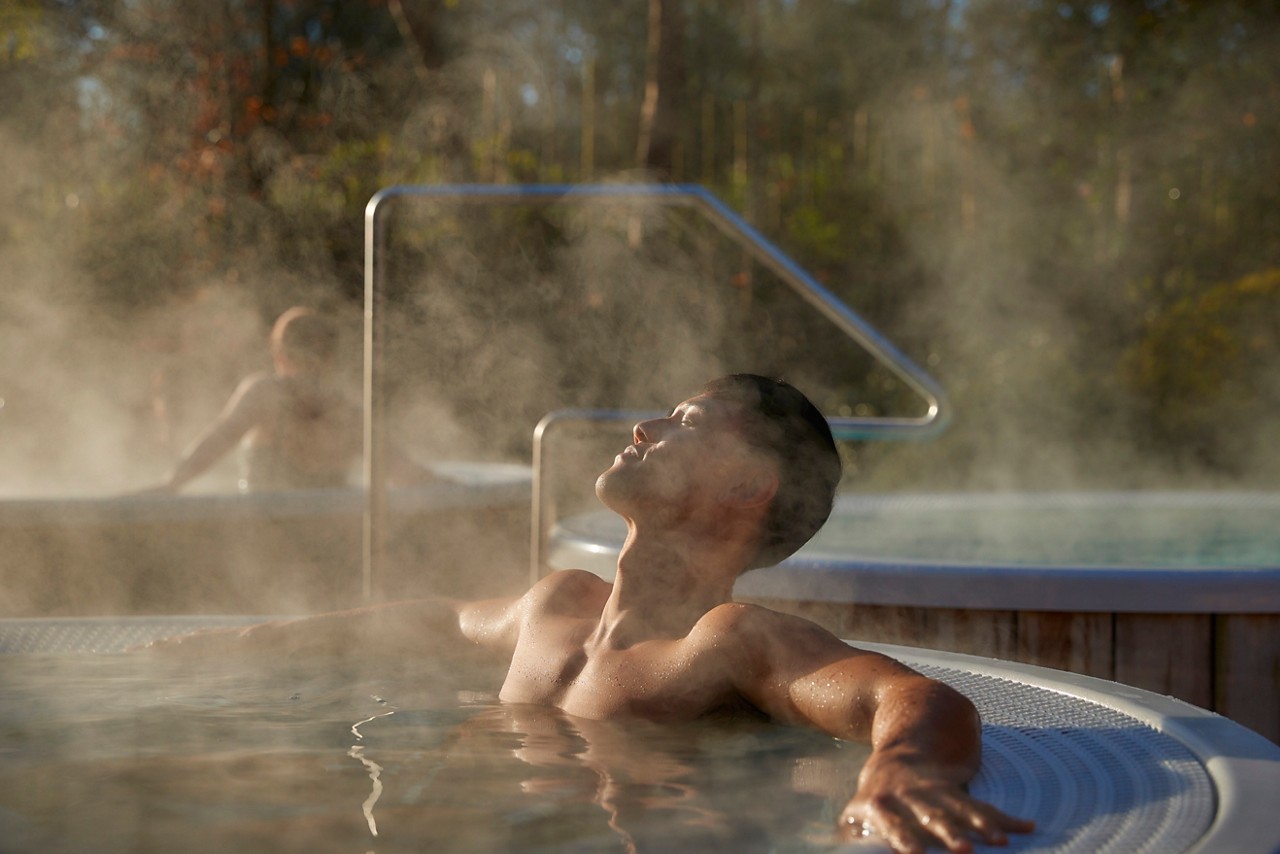 Man relaxing in an outdoor hot tub surrounded by the forest.