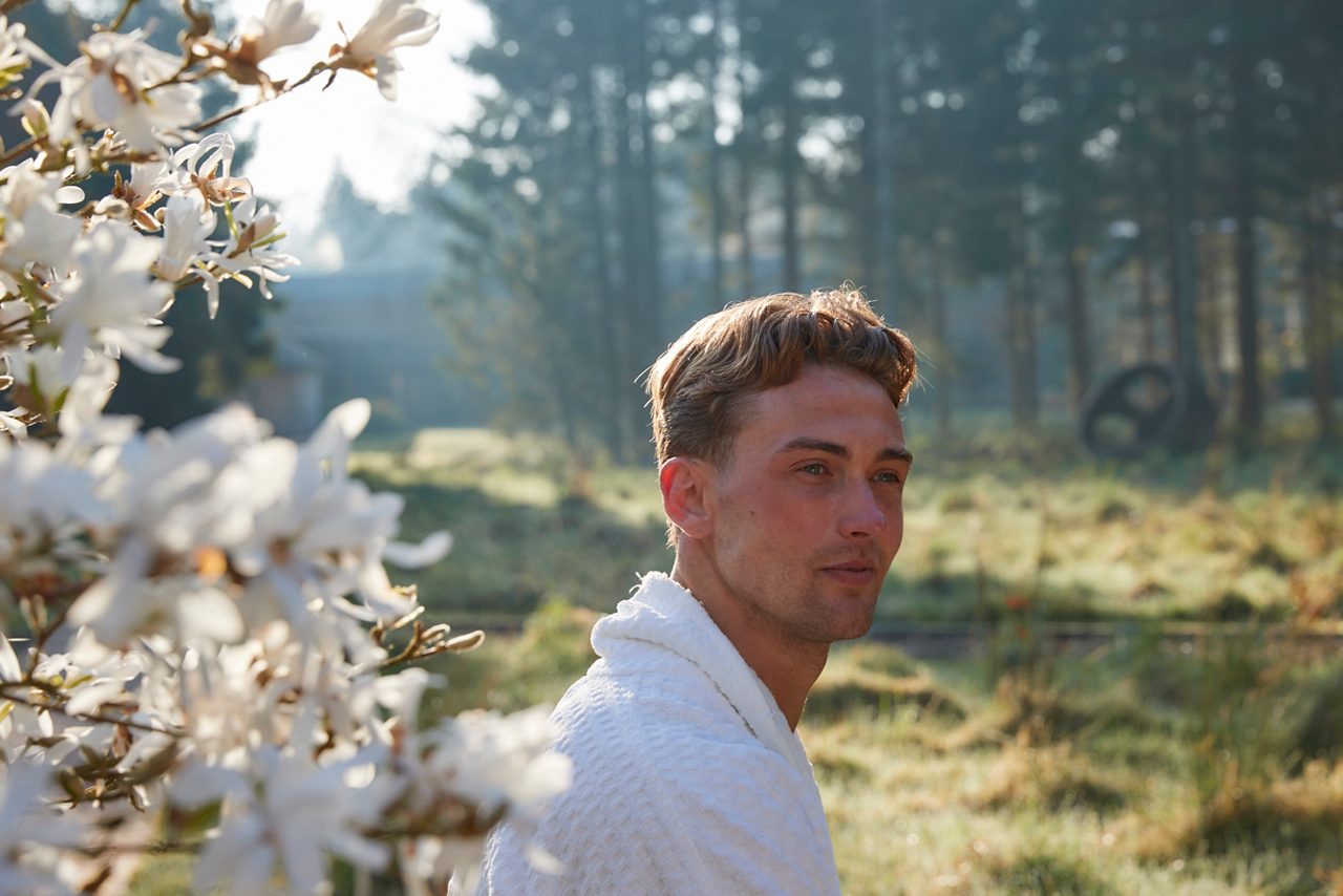 A man in a spa robe outside next to a blossom tree with forest trees behind him