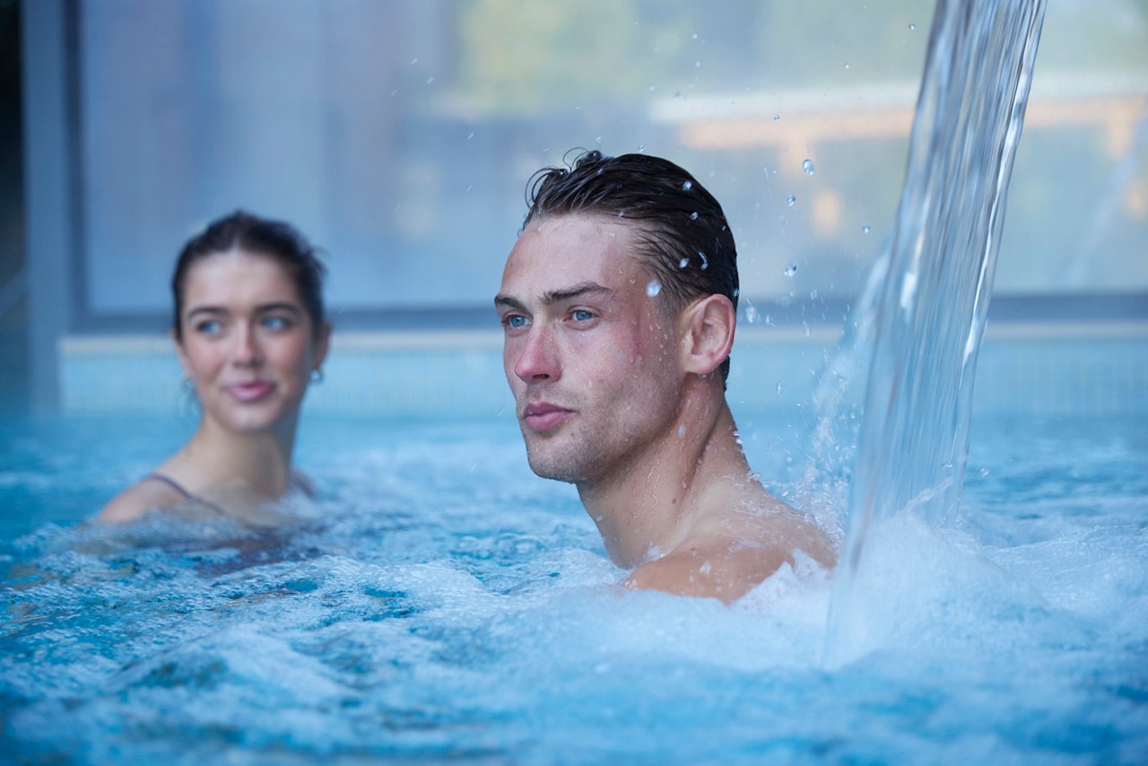 man under the water jet in the pool