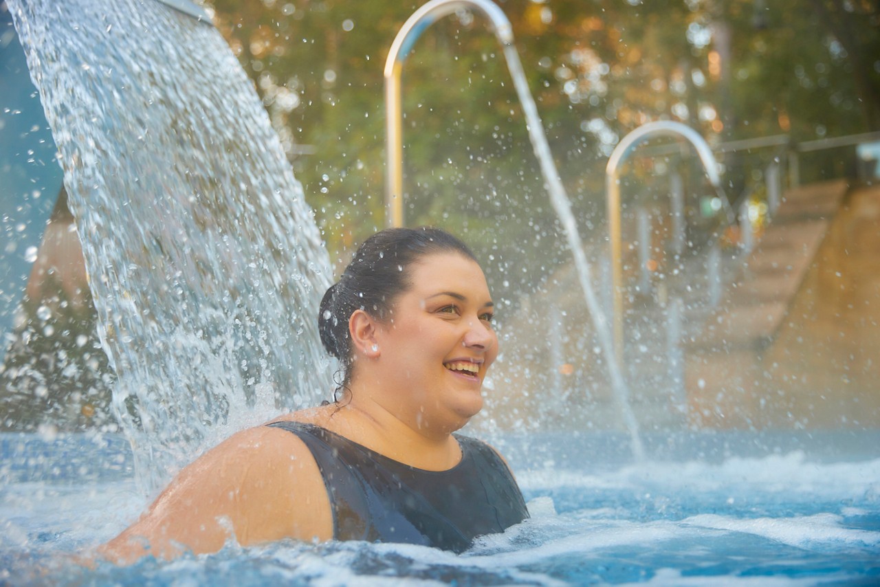 Women un a black swimsuit in a an outdoor pool surrounded by forest
