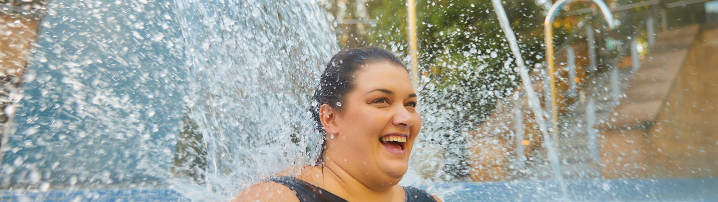 a women in an outdoor pool smiling with water flowing behind her
