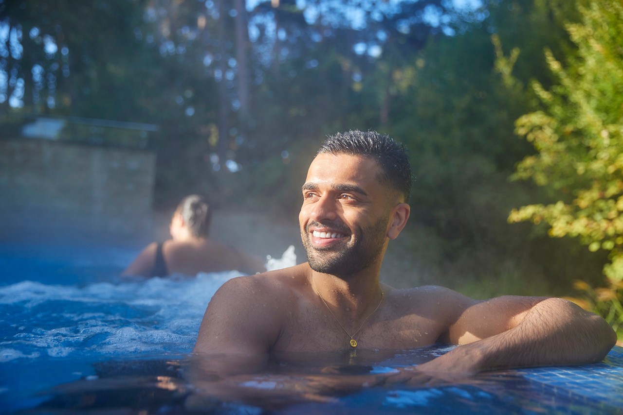 Man soaking in an outdoor pool surrounded by the forest.