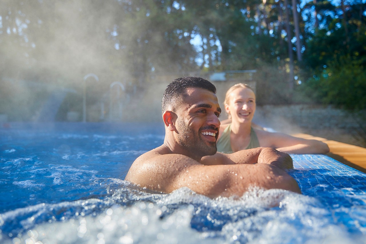 Couple soaking in an outdoor pool surrounded by the forest.
