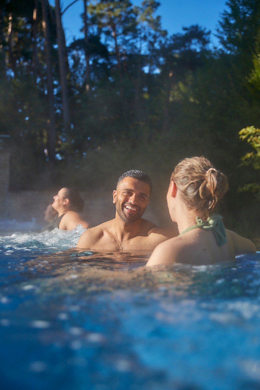Couple soaking in an outdoor pool surrounded by the forest.