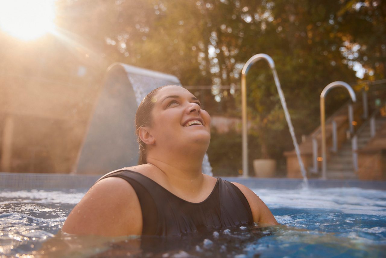 Woman soaking in an outdoor pool surrounded by the forest.