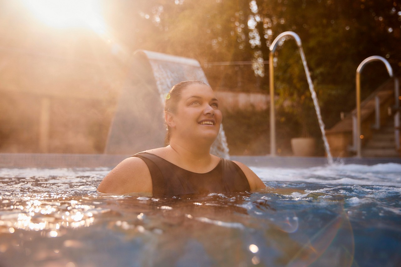 A lady relaxing in the outdoor pool with the sun rising behind her.