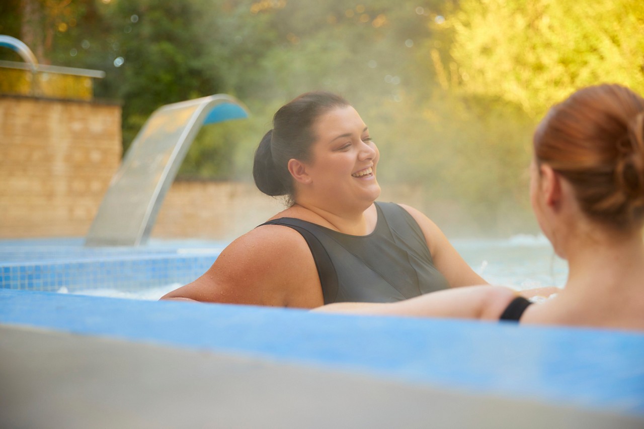 two women in black swimsuits in an outdoor pool smiling