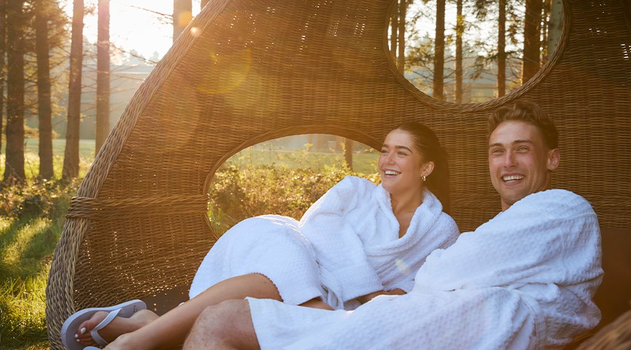 Couple snuggled in a large, cosy cocoon chair in the forest.