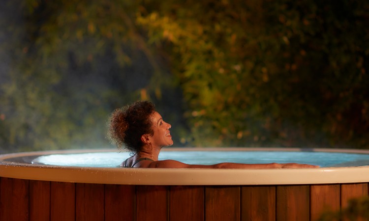 Woman soaking in an outdoor hot tub surrounded by the forest.
