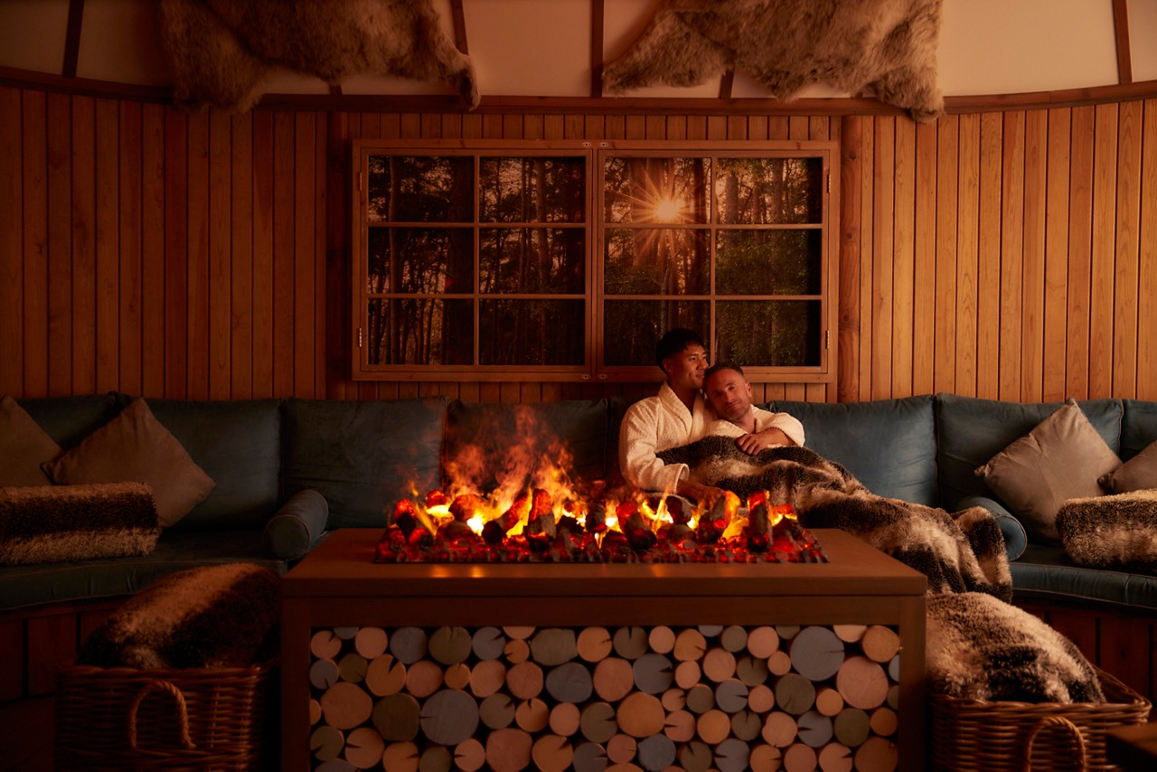 Couple snuggled up on a sofa in front of a fire inside the Scandianavian Snug. 