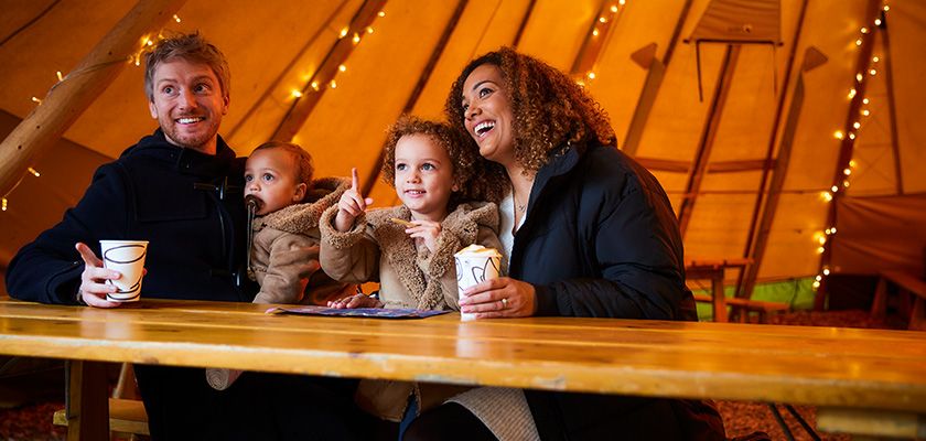 young family sat in twinkling Tipi with hot drinks 