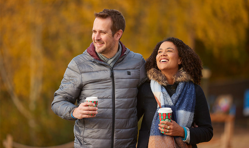 A couple walking together with coffee in their hands.