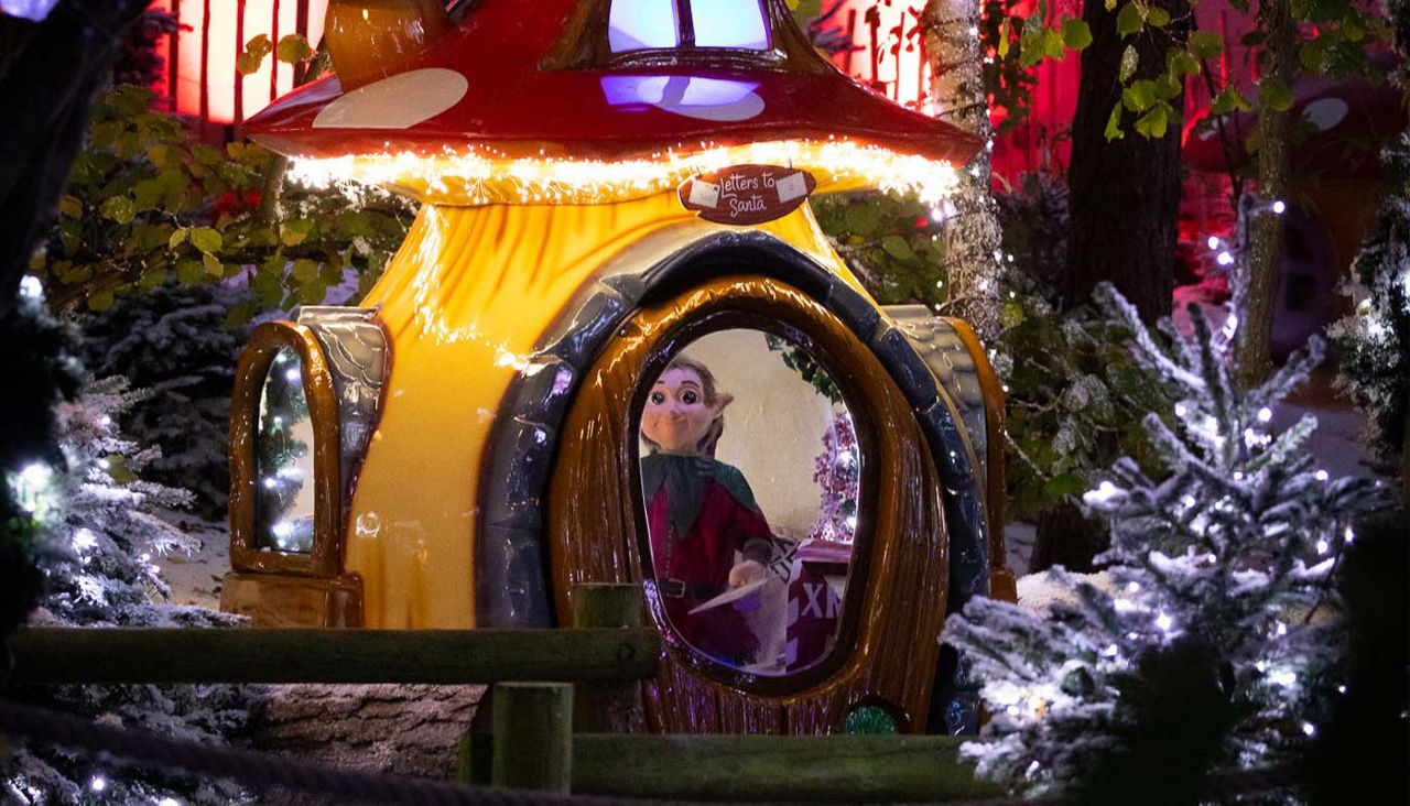 Toadstool lit up with animatronic elf inside surrounded by snowy trees